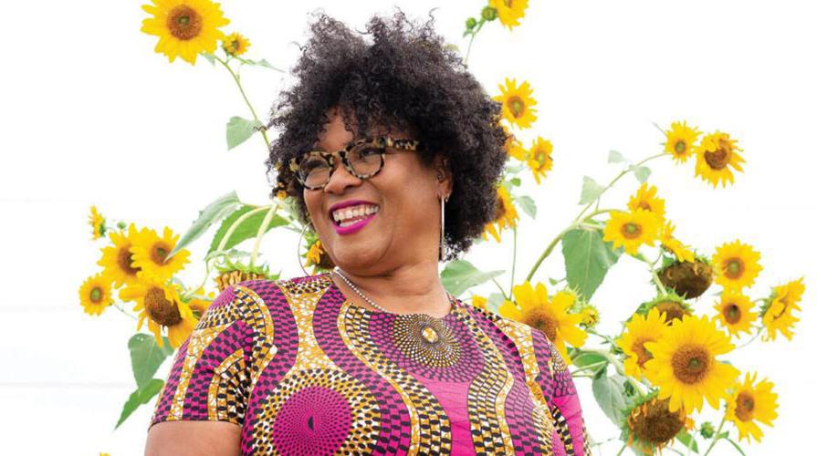 Monica 白色 headshot in a colorful dress in front of tall sunflower plants