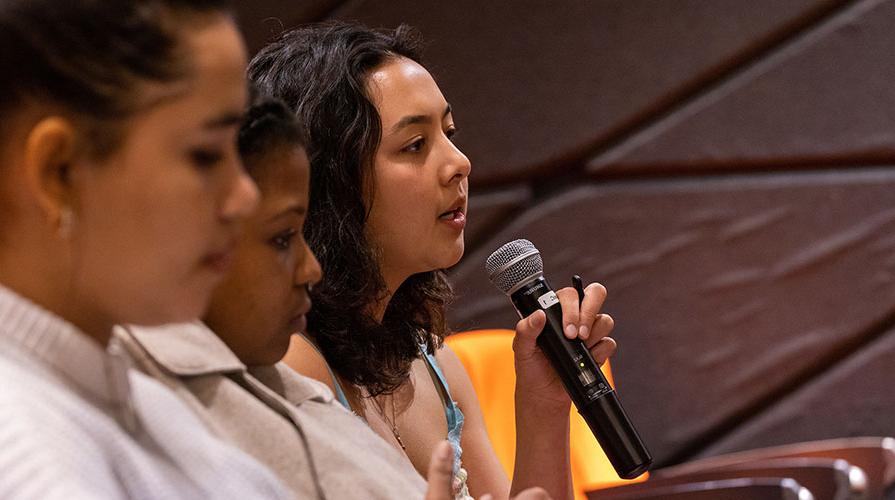 three seated students, one holding a mic and asking a question