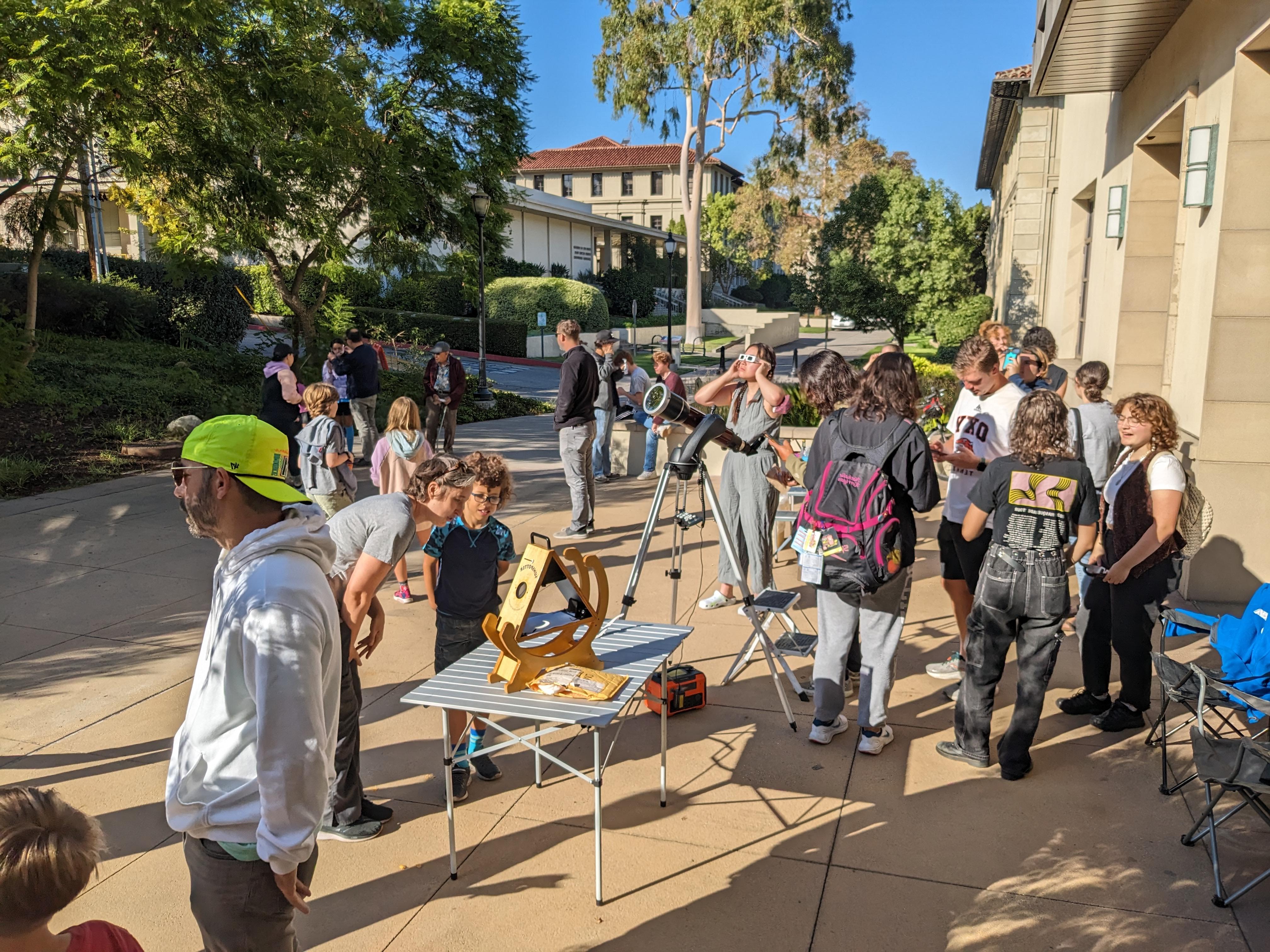 Oxy faculty, staff, students, and members of the local community standing around a telescope and sunspotter. Some are wearings solar eclipse glasses and looking at the partial solar eclipse.