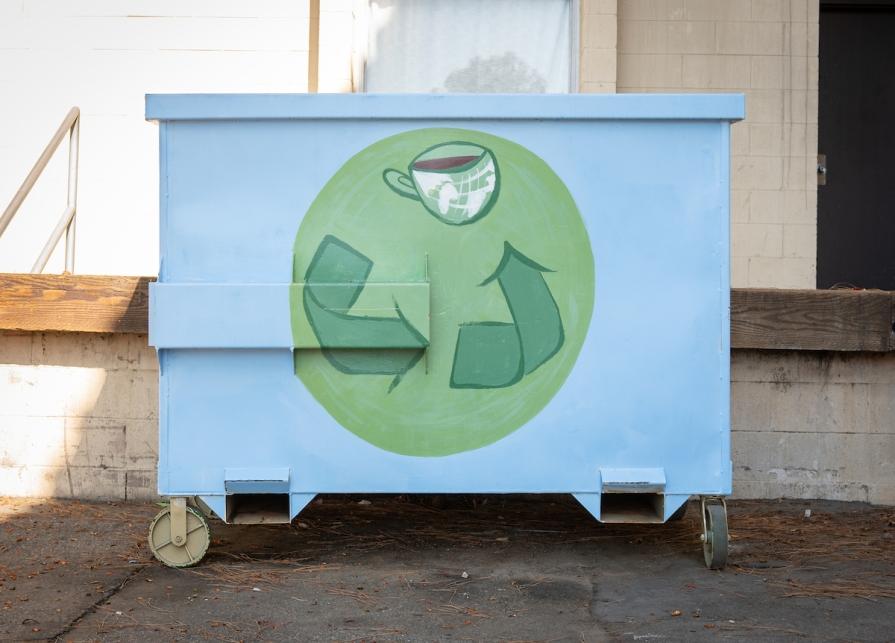 Dumpster painted with a blue background and green Recycle "chasing arrows" symbol on it.