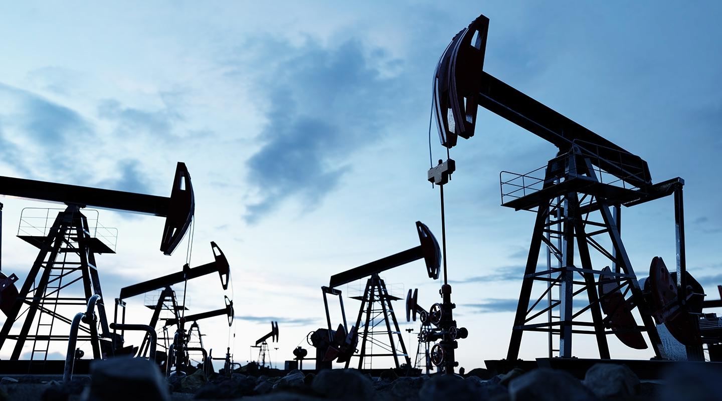 a series of silhouetted oil rigs against a blue, cloudy sky