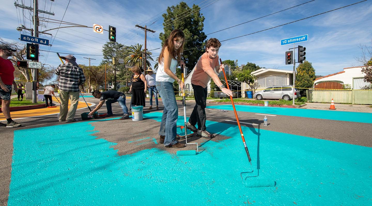 Two students painting the asphalt on Yosemite Way a bright teal color