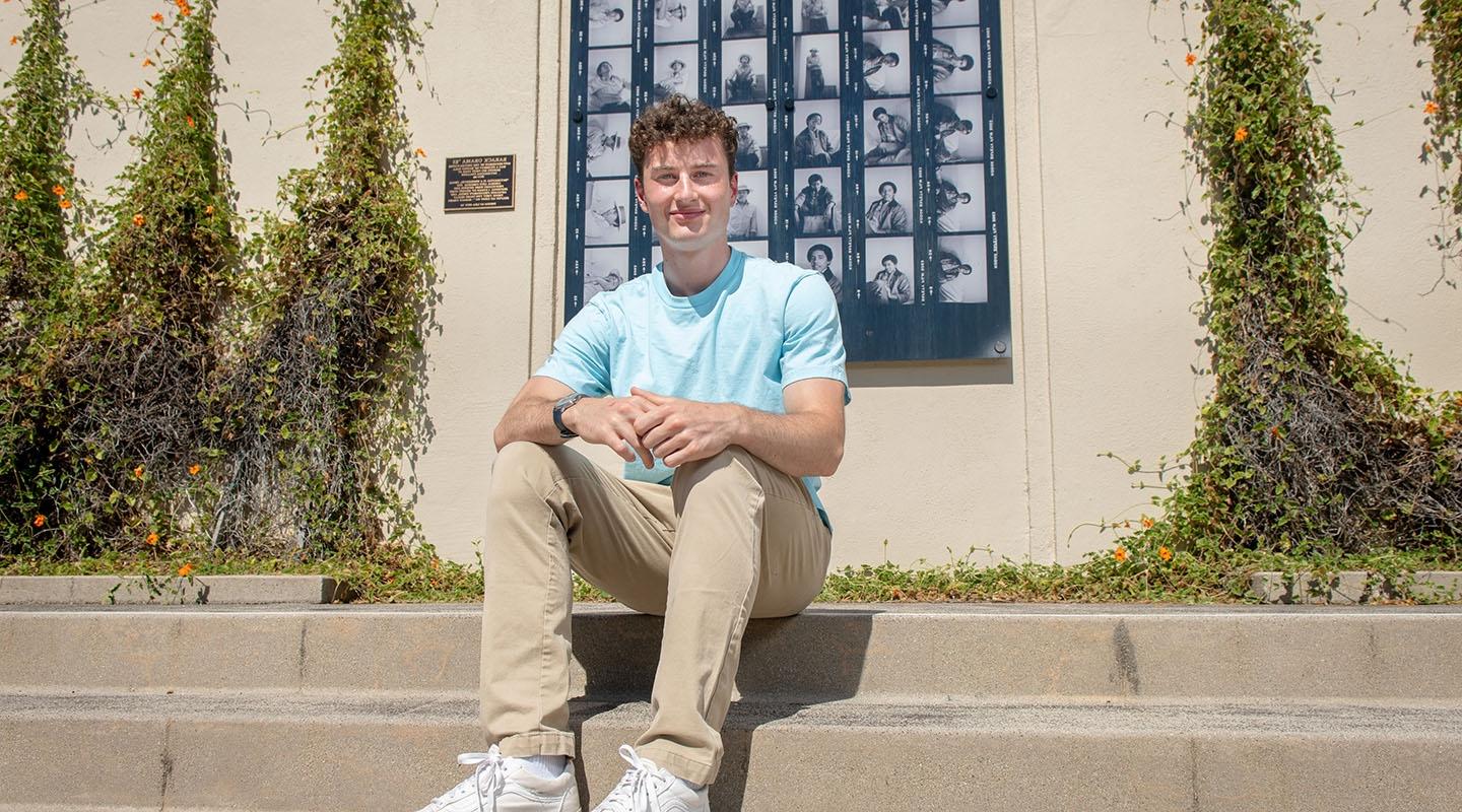 James 斯坦伯格 '25 sits on the steps in front of Haines Hall with a blue shirt.