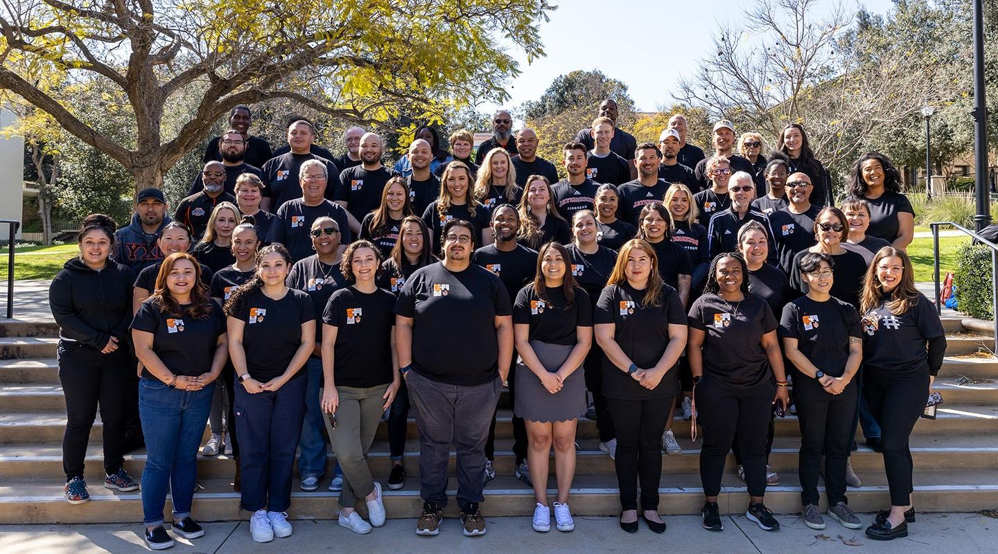 A large group of Student Affairs staffers standing on the steps on campus in black tshirts