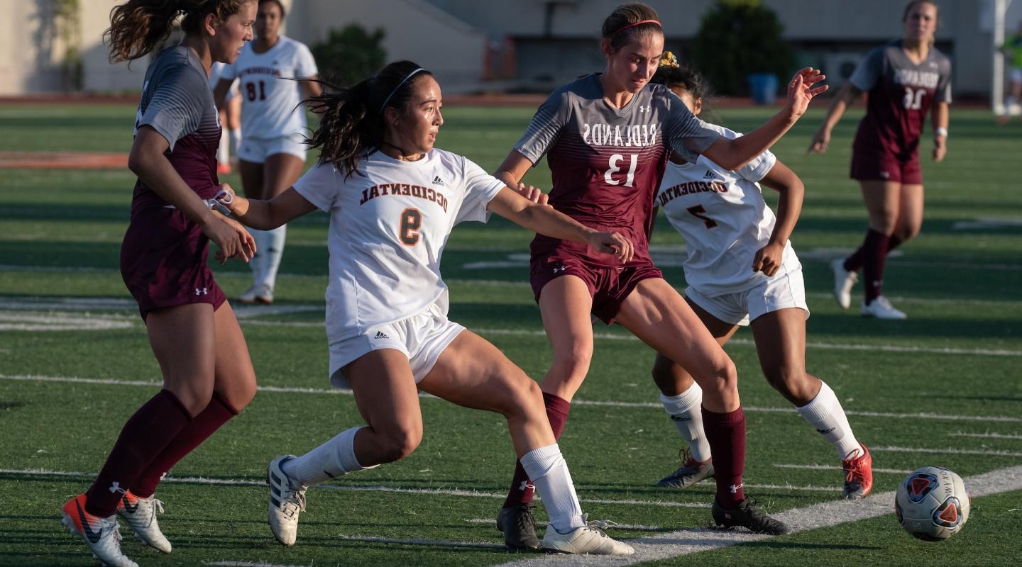 Four women playing soccer on turf field during daylight