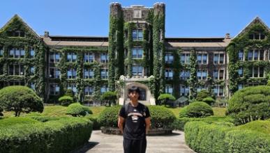 Hunter Leong stands in front of a university building in Korea whose walls are covered by moss