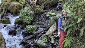 Dr. Greta Binford on a hillside with plants and a stream