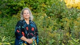 Robin Wall Kimmerer photographed outdoors in front of a green setting with wildflowers