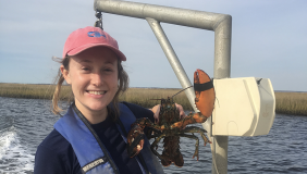 Zoe Kitchel stands on a boat holding a lobster specimen