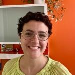 Laura is smiling and standing in front of an orange-red wall